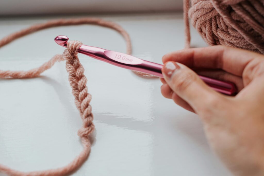 Hand holding crochet hook with pink yarn, showcasing a crafting process.
